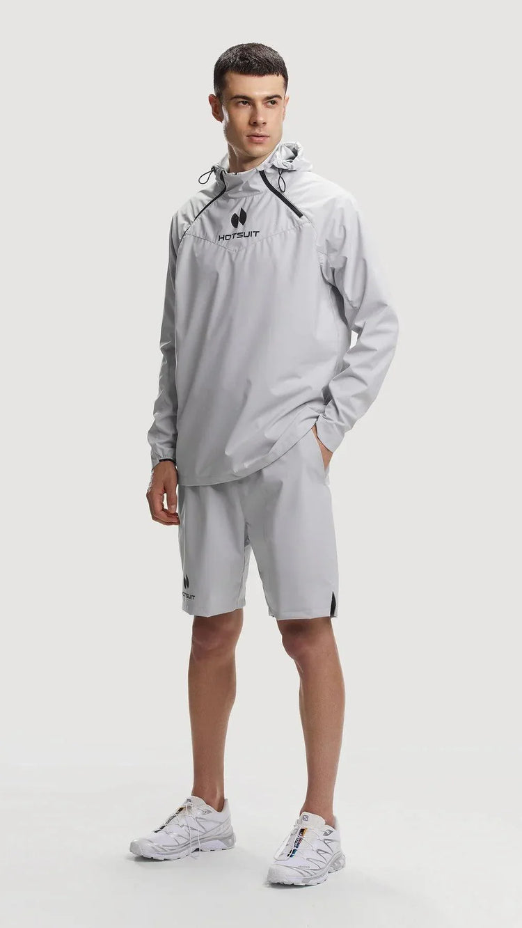 Man wearing gray HOTSUIT temp control sauna suit with hoodie and shorts, standing on white background
